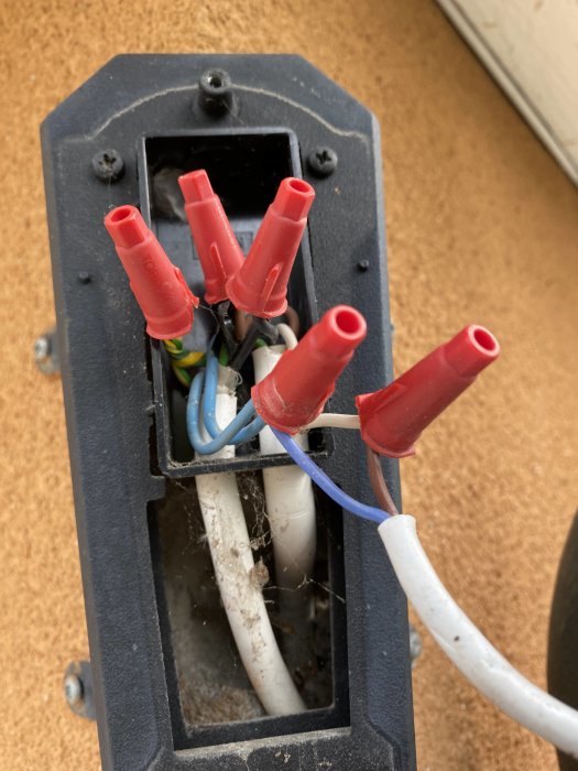 Öppen elarmatur med röda kopplingar och ledningar som leder ner till en sensor.
