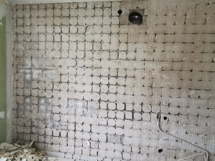 Væg med fjernet kakle og rester af fix, synliggør underliggende murværk med forskellig forfatning fra hjørne til centrum, kabler ses i nederste hjørne.