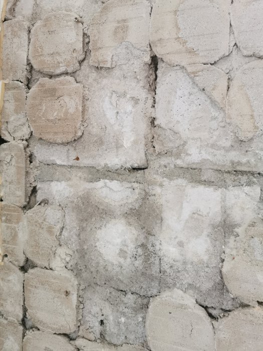 Væg af mursten med ujævn overflade, viser tæt lagte runde sten. Tidligere butik, nu sovrum. Ingen isolering bagved.