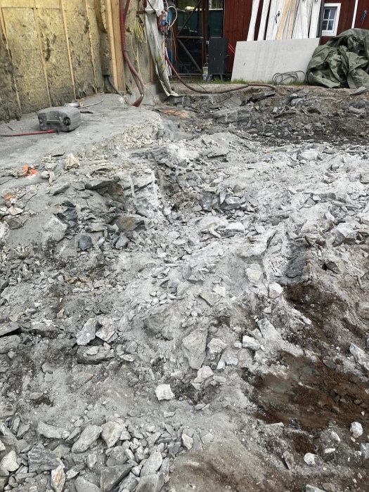 Rivningsområde med utspridda stenblock och grus nära byggnadsfasad och verktyg.