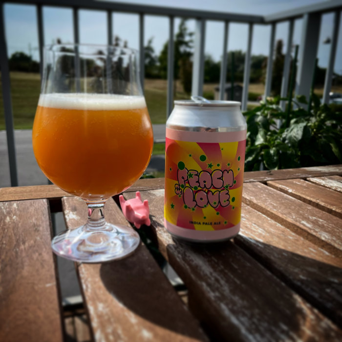 Ett glas öl och en ölburk på ett bord, bredvid en liten rosa plastleksaksgris som ligger på rygg.