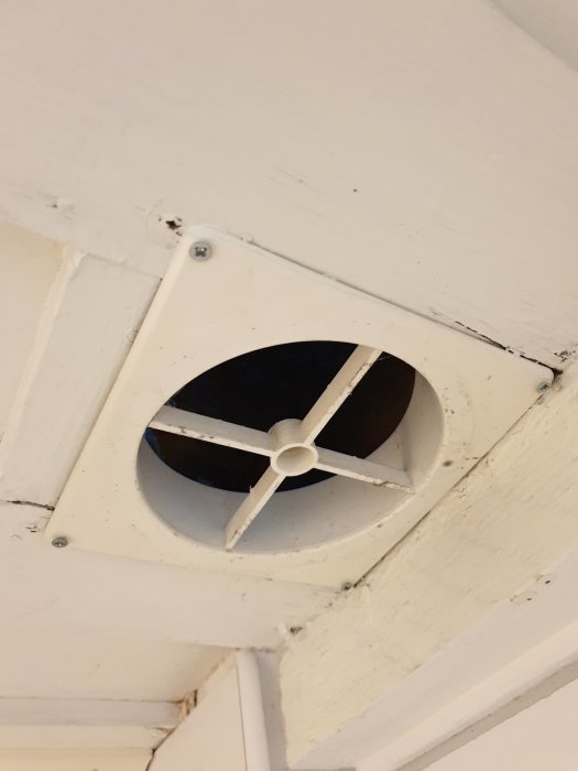 Bild på en öppen tallriksventil i ett badrumstak, visar synlig isolering och utrymmet runt ventilkanalen.