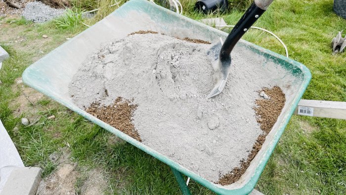 Blandning av gjutgrus och cement i en skottkärra med spade, redo för användning vid byggprojekt.