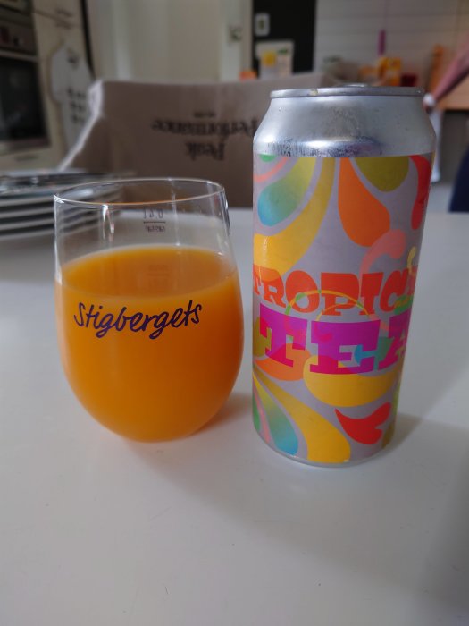 Burk med tropiskt mönster bredvid ett glas fyllt med orangefärgad dryck, på burken texten "TROPICAL".