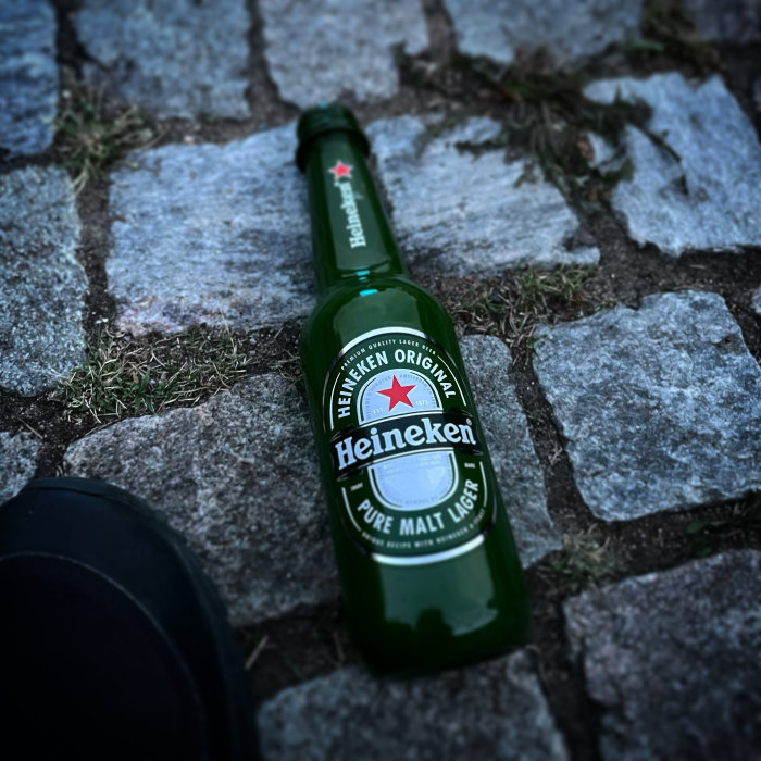 Grön Heineken ölflaska liggande på stenlagd mark.