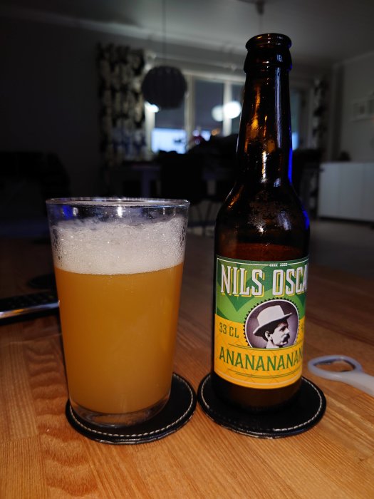 Ölflaska och ett glas med skummande öl på ett bord i ett vardagsrum.