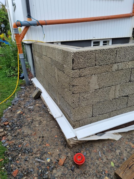 Ny utbyggd källarvägg 4.5 cm innanför befintlig fasad, med temporärt rör och byggmaterial synliga.