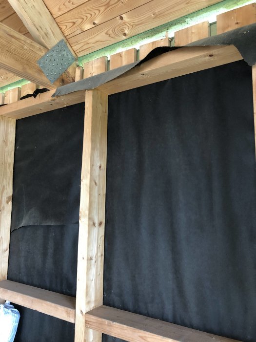 Isoleringsarbete i gästhus med vindpapp och träreglar på en vägg.