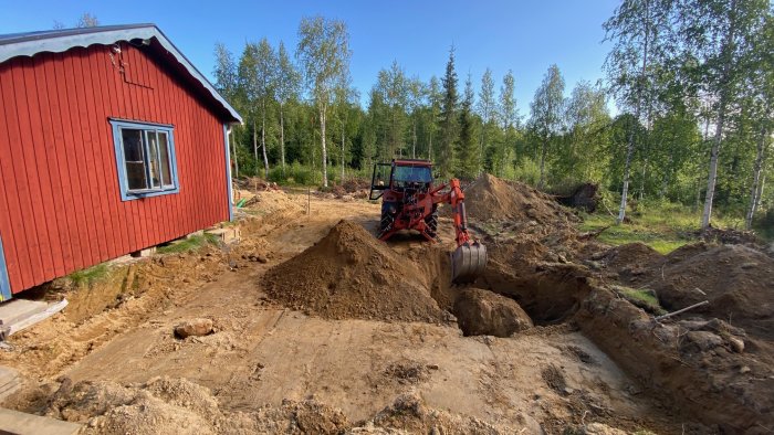 Utgrävning vid hus för tillbyggnad med grävmaskin och synlig stor sten.