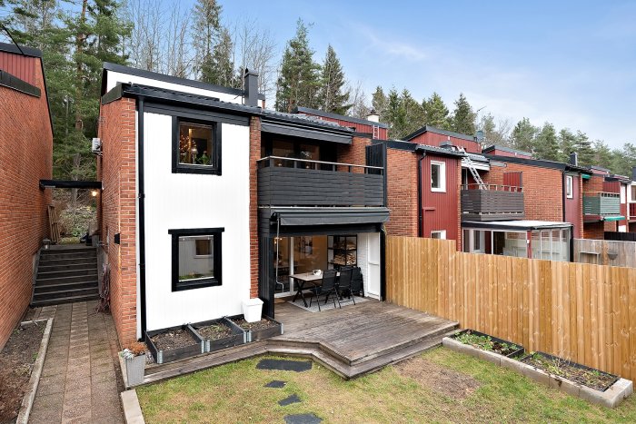 Kedjehus i sutteräng med 4 halvplan, trädäck och balkong, omgivet av andra hus och natur.