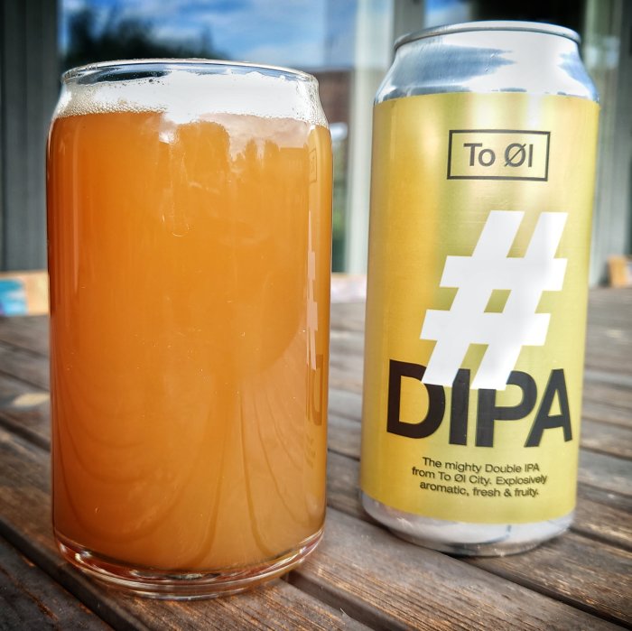 Ett glas med grumlig, orange IPA-öl bredvid en burk med etiketten "#DIPA" på ett träbord.