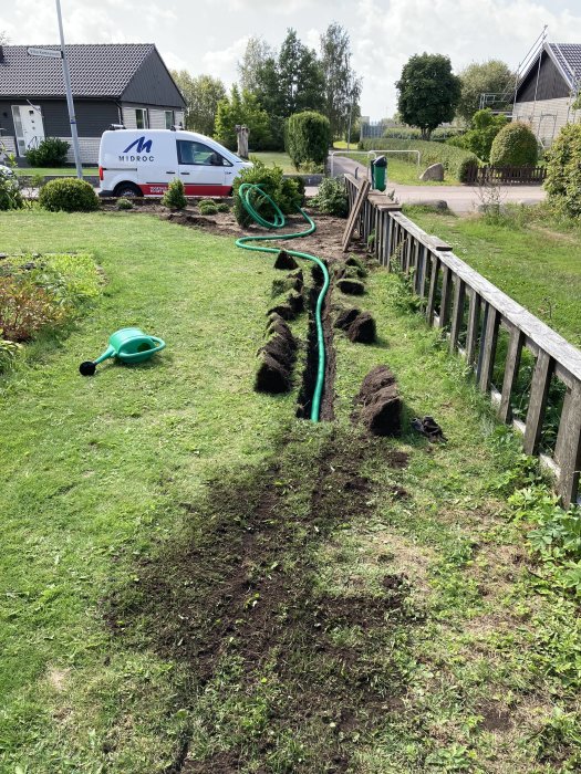 Uppgrävd trädgård med rör för fiberinstallation, grönt gräs och verktyg synligt.