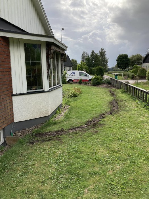 Trädgård vid hus med nedsågad barrbuske och grävd mark för fiberinstallation mot bakgrund av gata.