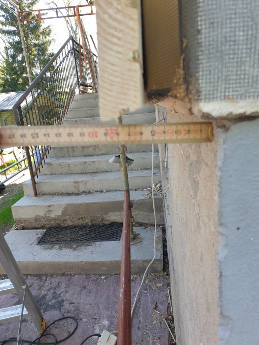 Måttband visar avstånd mellan sockel och ytterpanel vid en husfasad under renovering.