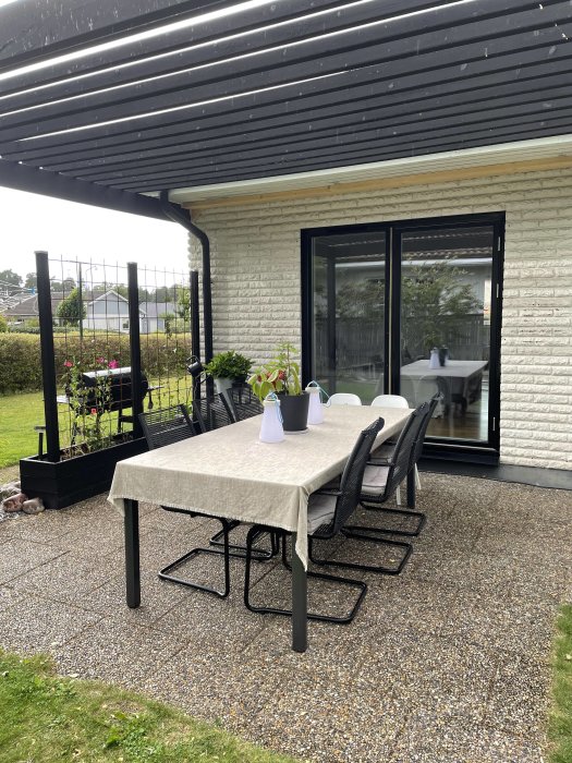 Husfasad med nya svarta aluminiumfönster som går ner till golvet, omgiven av trädgårdsmöbler på en stenlagd terrass.