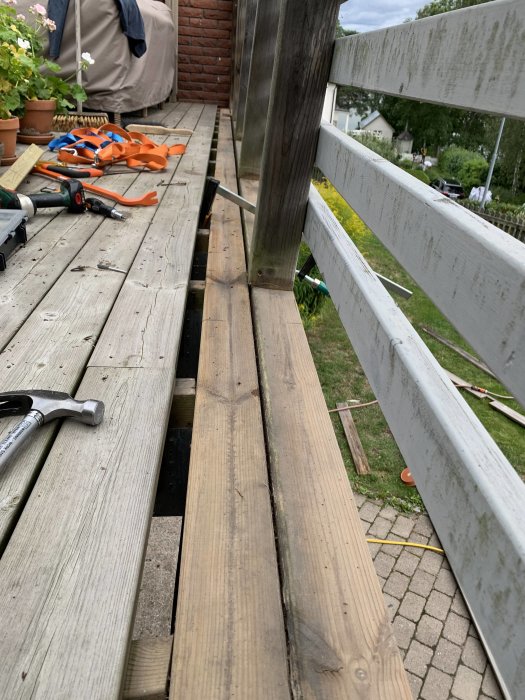 Skev limträbalk på altan med skruvar och verktyg runtomkring, samt trall där skarven exponeras.