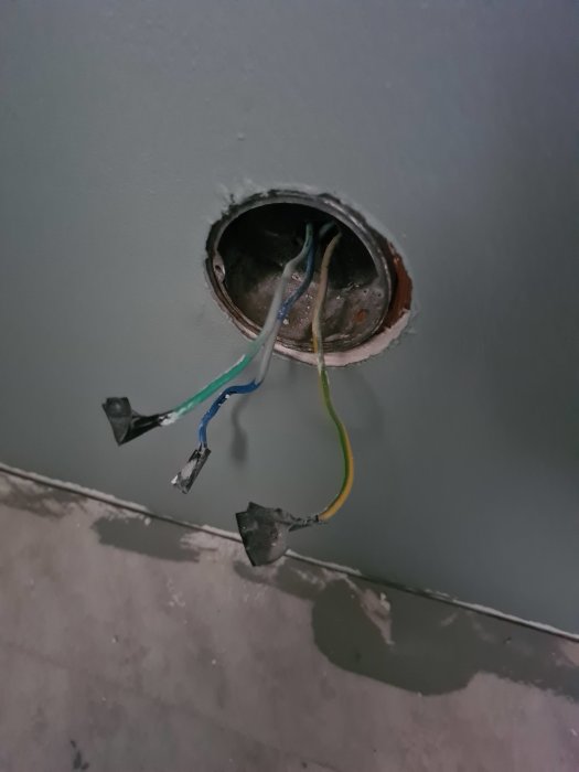 Eluttag under renovering med tre elledningar, en med grön-gul rand, genom en väggöppning.