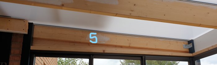 Uterum med träbjälkar och isolerat tak, numrerad yta 5 ovanför ett glasparti.