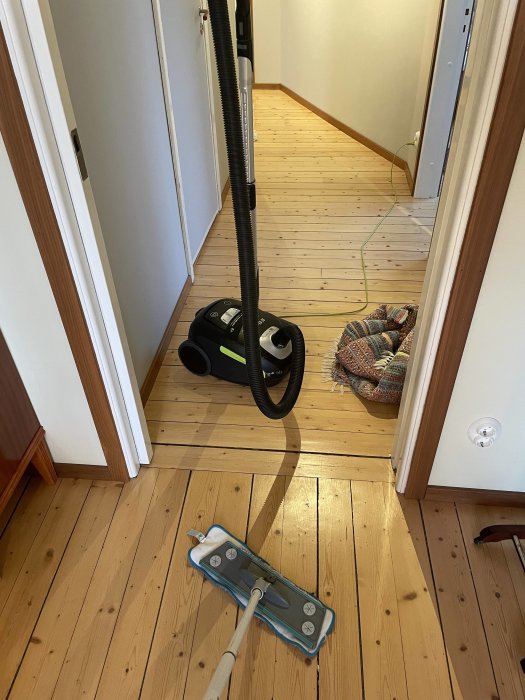 Dammsugare och mopp på ett trägolv i en korridor under en pågående dammsanering.