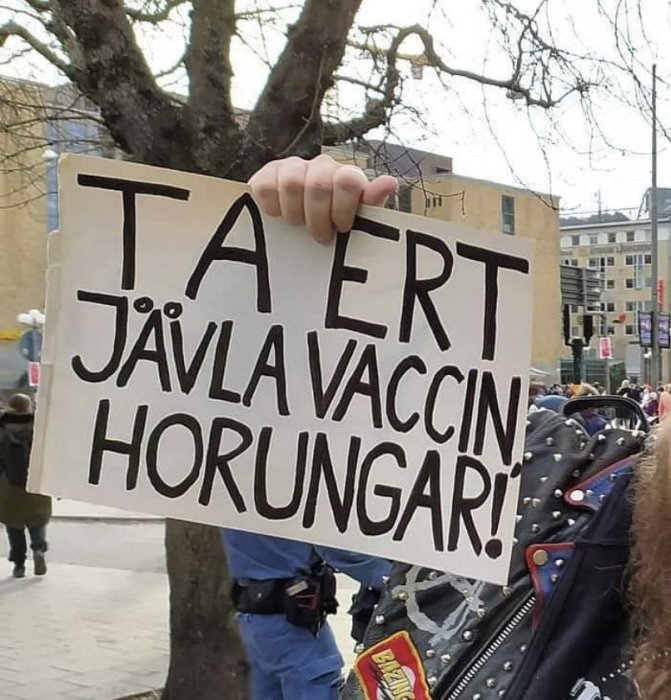 Person håller skylt med uppmaning att ta vaccin under protest eller demonstration.