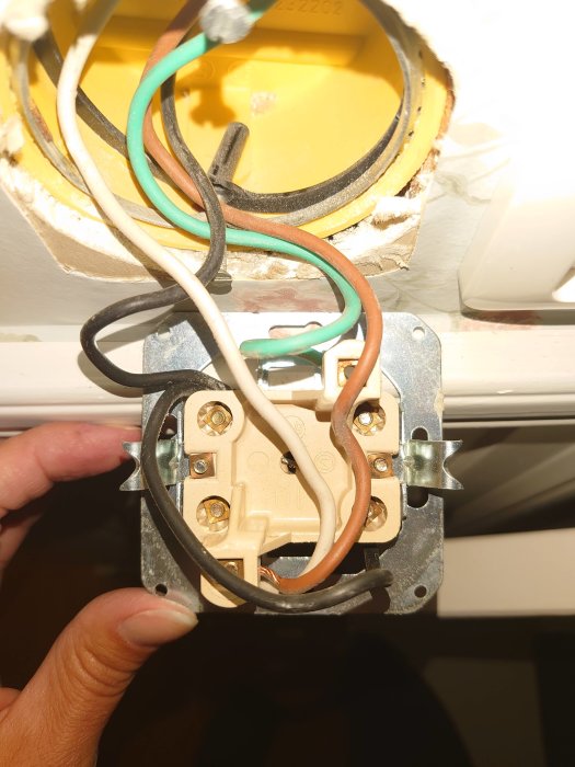Närbild av en person som håller i en elektrisk brytare med anslutna kablar i en väggmonterad dosa.