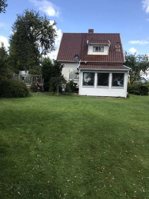 Ett enfamiljshus med gräsmatta och rött tegeltak, potentiellt för temporära träreparbeten.
