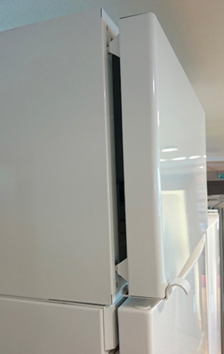 Vit överskåp från Ikea monterad på vägg i kök, dörr på glänt som visar konstruktion och gångjärn.