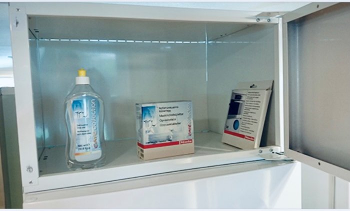 Ett vitt Ikea överskåp öppet med en flaska och två kartonger från Miele inuti.