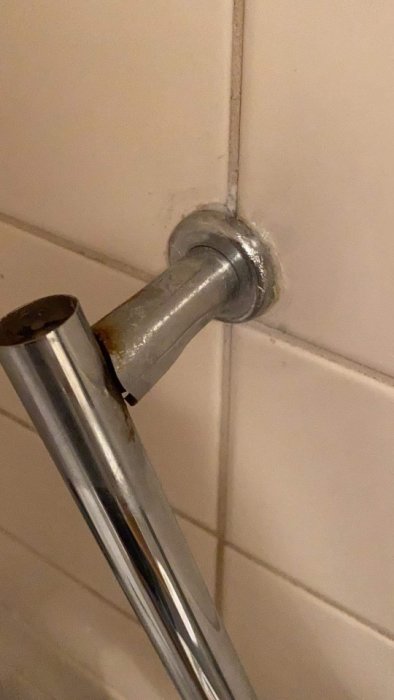 Rostig duschstång fäst i kaklad vägg med snurrande otydlig fästning.