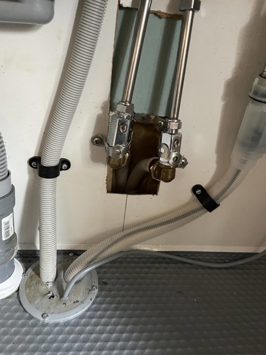 Vattenledningar och klammer under diskbänk efter åtgärdat vattenläckage, med inböjda rör i väggen.