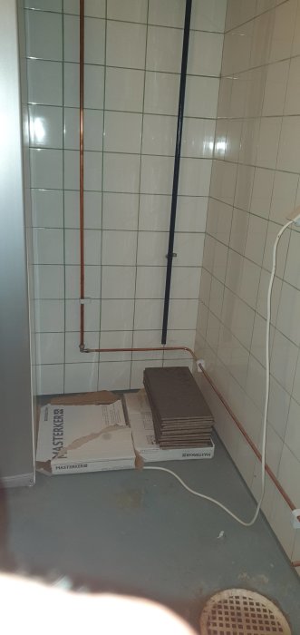 Kopparrör förlängt att sluta ovanför golvbrunnen i ett hörn av ett kaklat utrymme med byggmaterial.