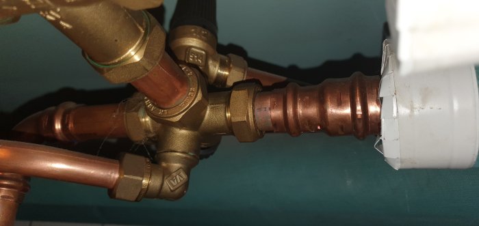 Koppar och mässingsrör med 90-graders vinkel över golvbrunn, diskuterar överskottsvatten från värmepump.