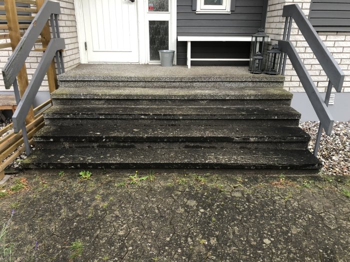 Ett slitet trappräcke i grått vid en husentré med stentrappa och mexitegel, behöver renovering.