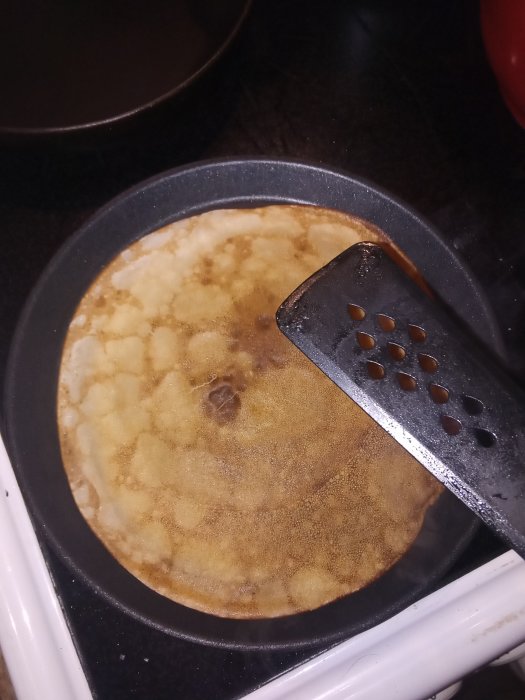 En pannkaka som steks i stekpanna med en svart stekspade.