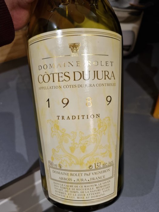 Flaska vintagevin från 1989 med etikett "Domaine Rolet Côtes du Jura", bärnstensfärgat, i närbild.