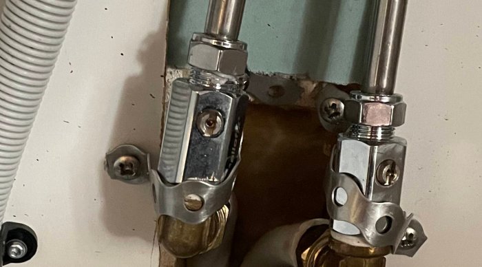 Närbild på röranslutningar med metallfästen och en oklar del som sticker fram.