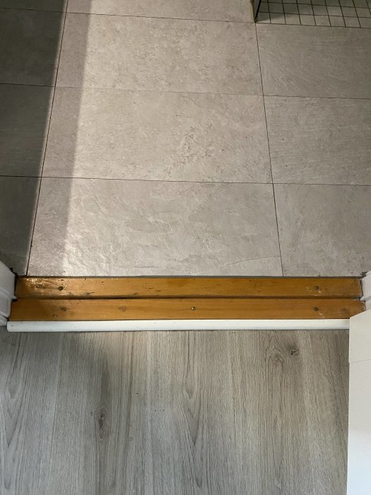 Tröskel i trä mellan ett badrums kakelgolv och ett laminatgolv som behöver ommålning.