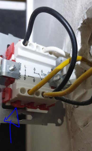 Öppen strömbrytare i vägg med två vippor, anslutna kablar och blå pil som pekar på en vippan.