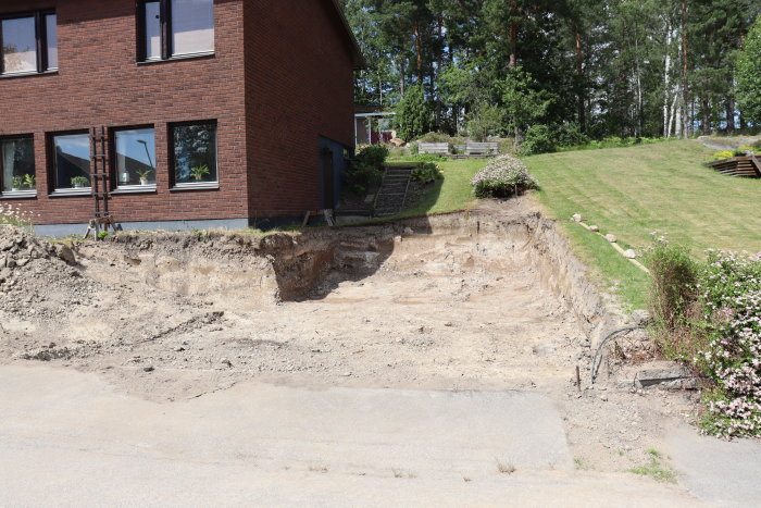 Uppgrävd jord på tomt intill en väg och röd tegelvilla, med planer på gräsmatta och gångväg.