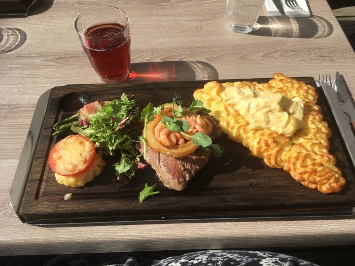 Plankstek med klyftpotatis, lökringar, räkor och sallad upplagt på träplanka bredvid ett glas rött.