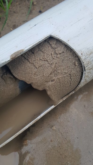 Ett avskuret rör fyllt med en blandning av sand, lerklumpar och småsten.