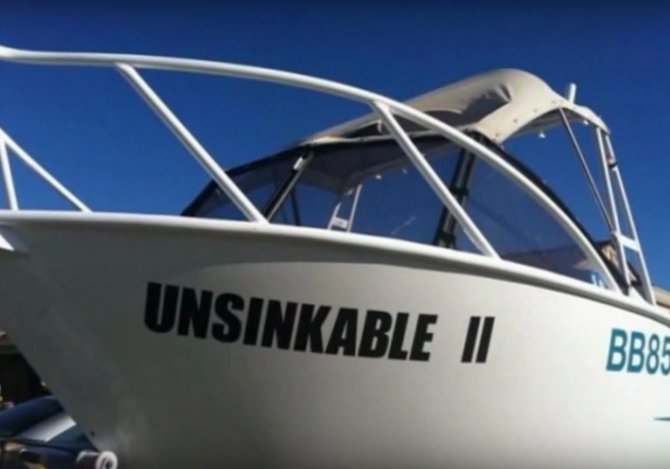 Vit motorbåt med texten "UNSINKABLE II" på sidan under klarblå himmel.