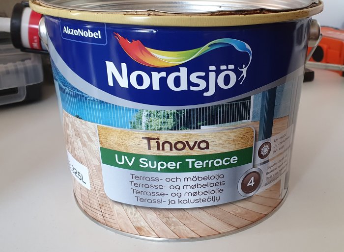 Burk med Nordsjö Tinova UV Super Terrace träolja framför suddig bakgrund av byggmaterial.