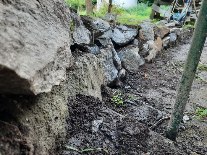 Nybyggd mur av oregelbundna sprängstenar i en trädgård, sett nära marknivå.