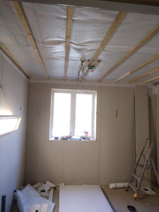 Interiör under renovering med osb-skivor på väggar, träreglar i tak och stege.