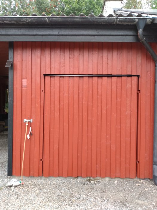 Modifierad röd garageport med jämnt linjerad panel, stängd, med en sopkvast lutad mot väggen.