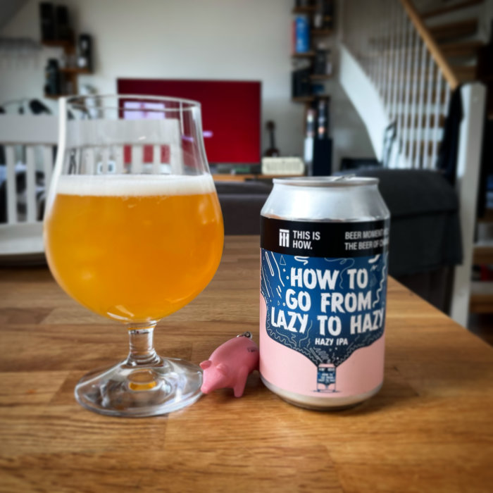 Ett glas med öl och en ölburk med texten "HOW TO GO FROM LAZY TO HAZY", med en liten plastgris framför, i ett vardagsrum.