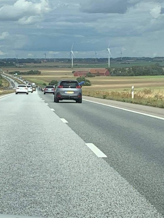 Bilar på motorväg med landskap och vindkraftverk i bakgrunden.