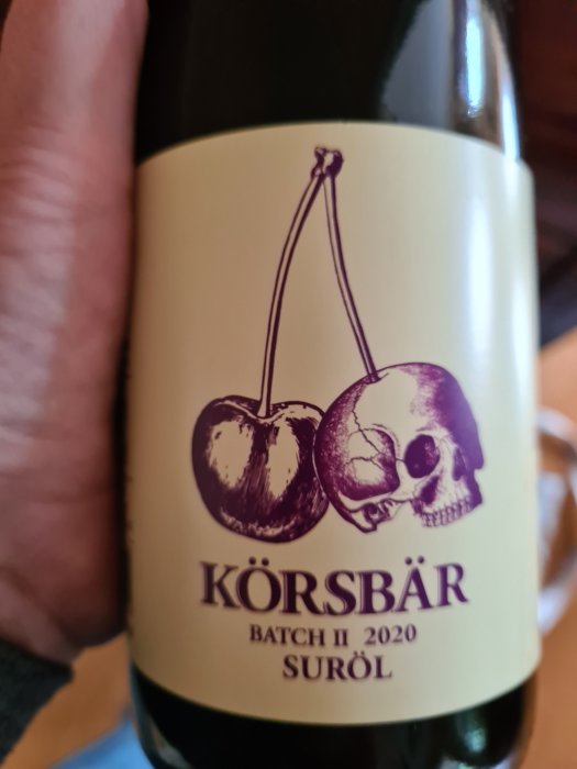 Flaska med etikett för suröl, "KÖRSBÄR BATCH II 2020", med bild av körsbär och dödskalle.