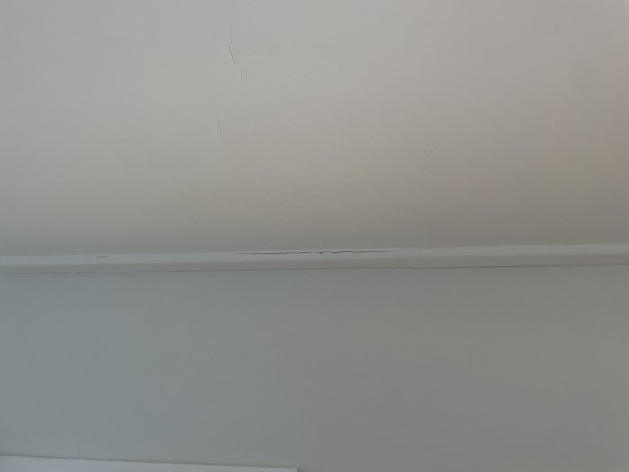 Vit vägg med sprickbildningar ovanför en list, tecken på potentiell strukturskada i äldre hus.